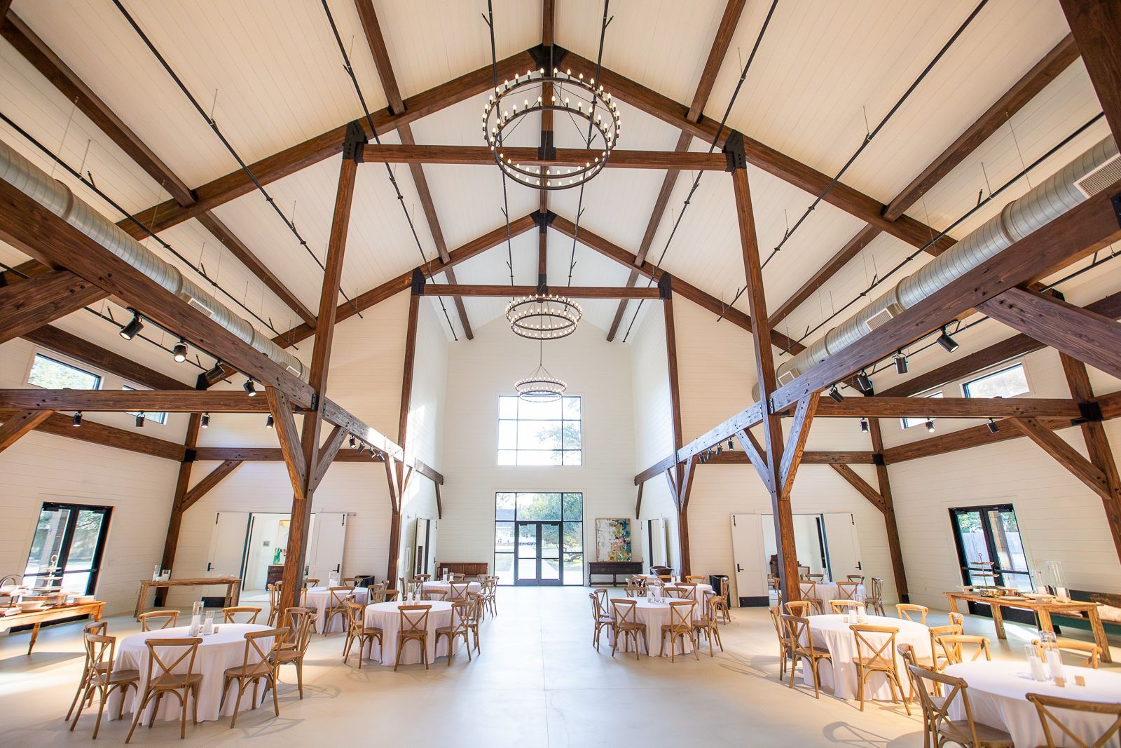 Event space with wooden beams, tables with pink linens, and decorative chandeliers.