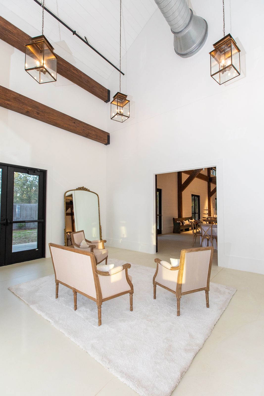 Bright white room with seating on a fluffy rug, a large mirror, and open doorway to another room.