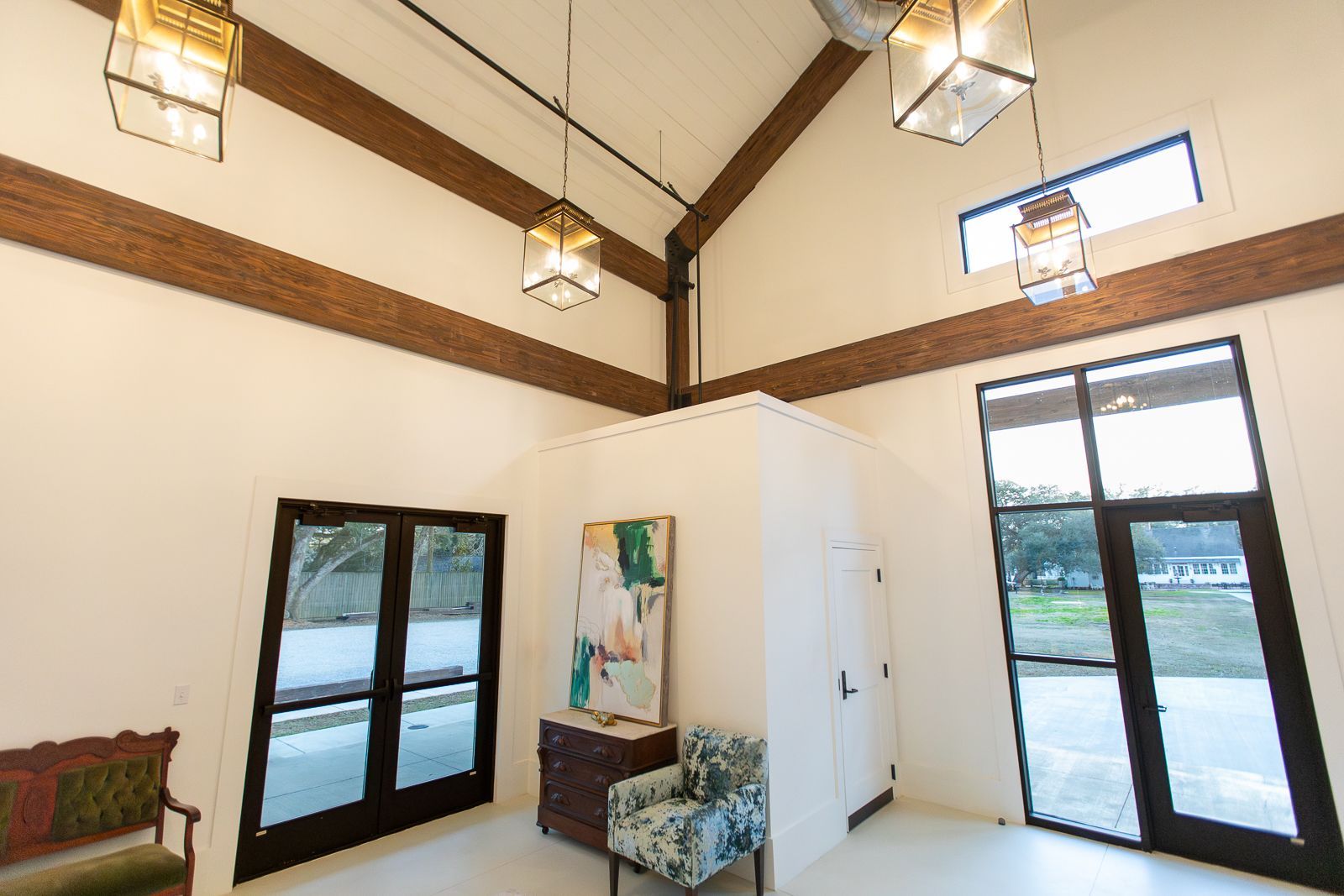 Bright, modern interior with vaulted ceiling, wood beams, and large windows. Art and seating are present.