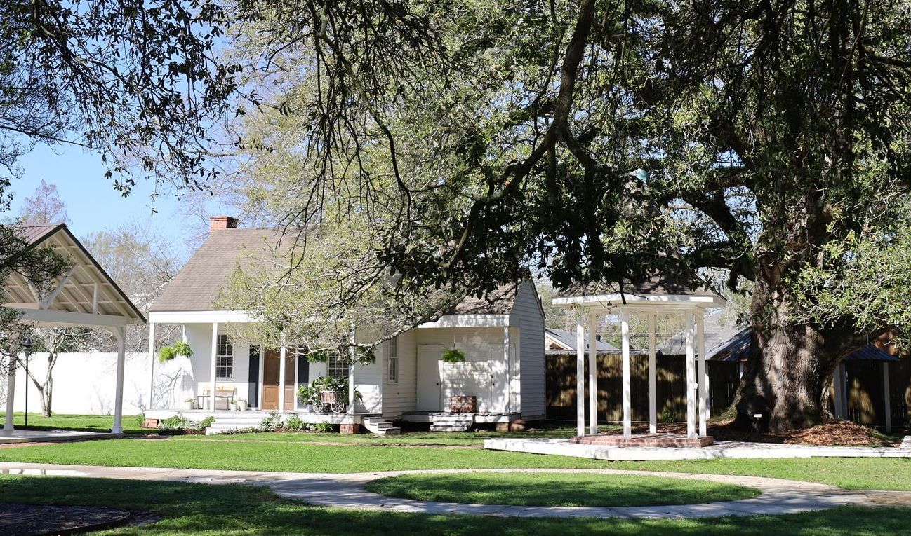 White historic house with porch, under a large tree, on a grassy lawn.