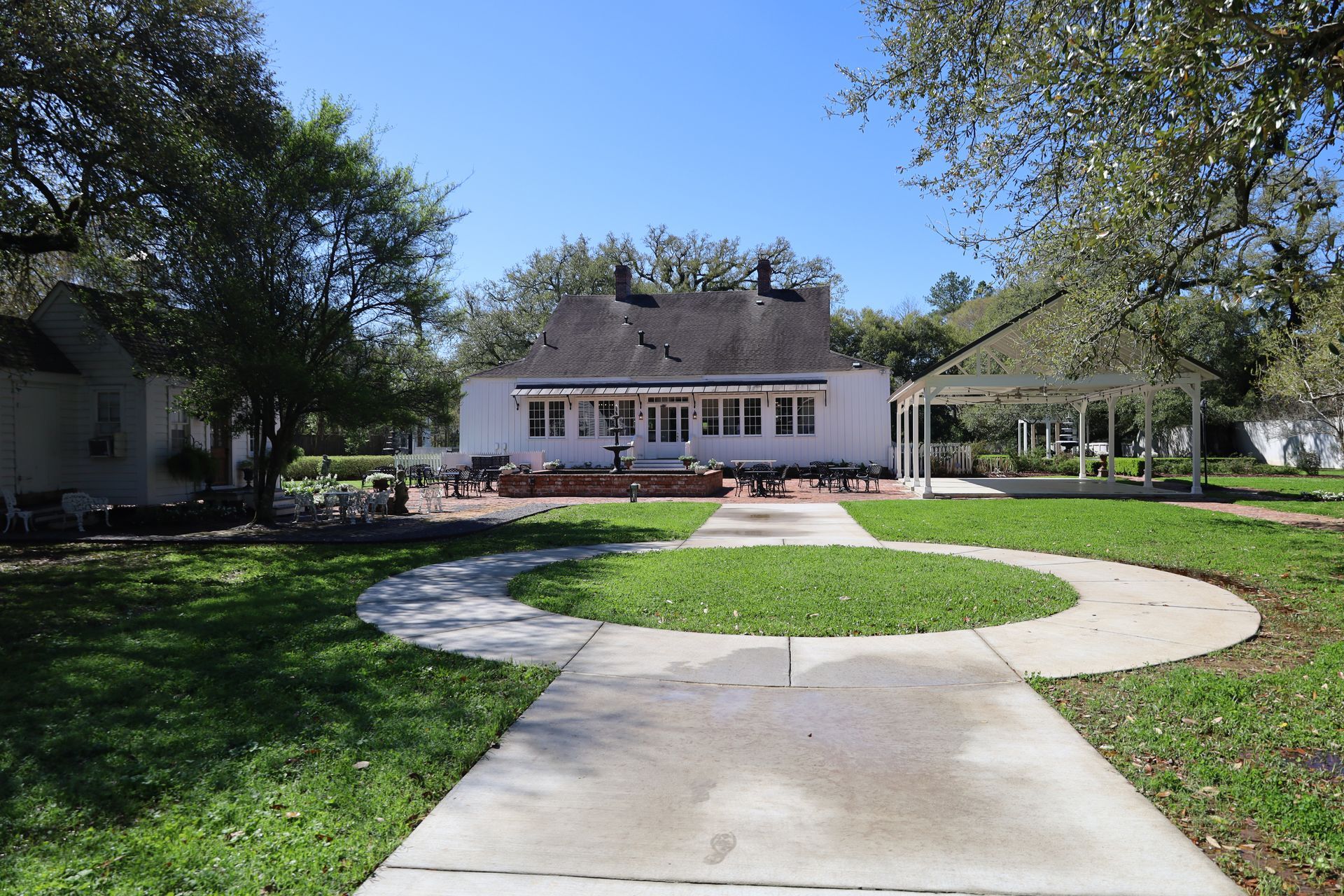 White house with a brick patio, walkway, and small pergola in a grassy yard under a blue sky.