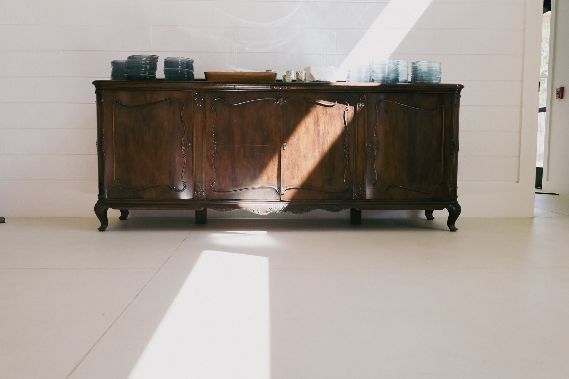 Wooden cabinet against a white wall. Sunlight casts shadows on the floor and furniture.