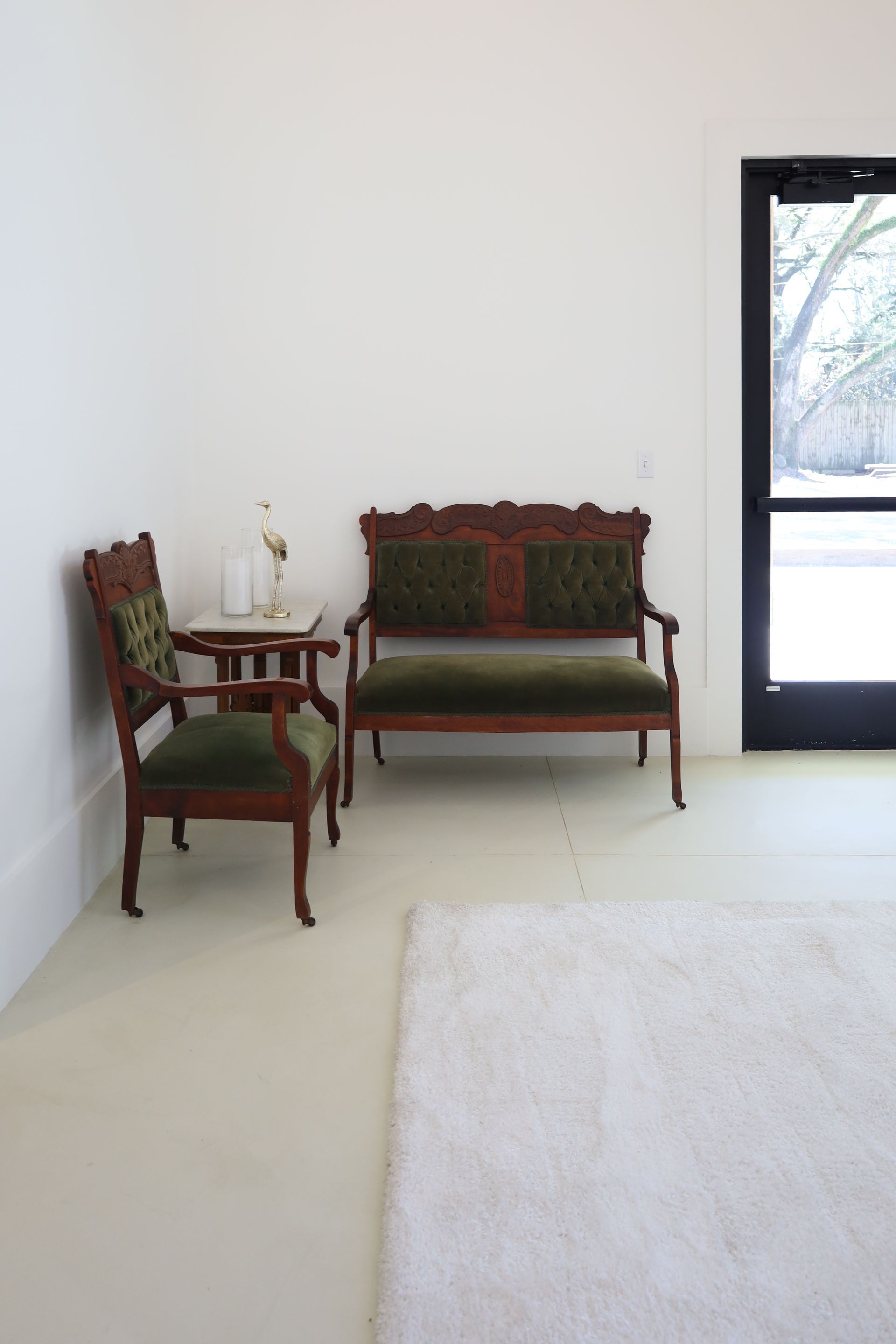 Green velvet antique sofa and chair beside a small table, set against a white wall; white rug on floor.
