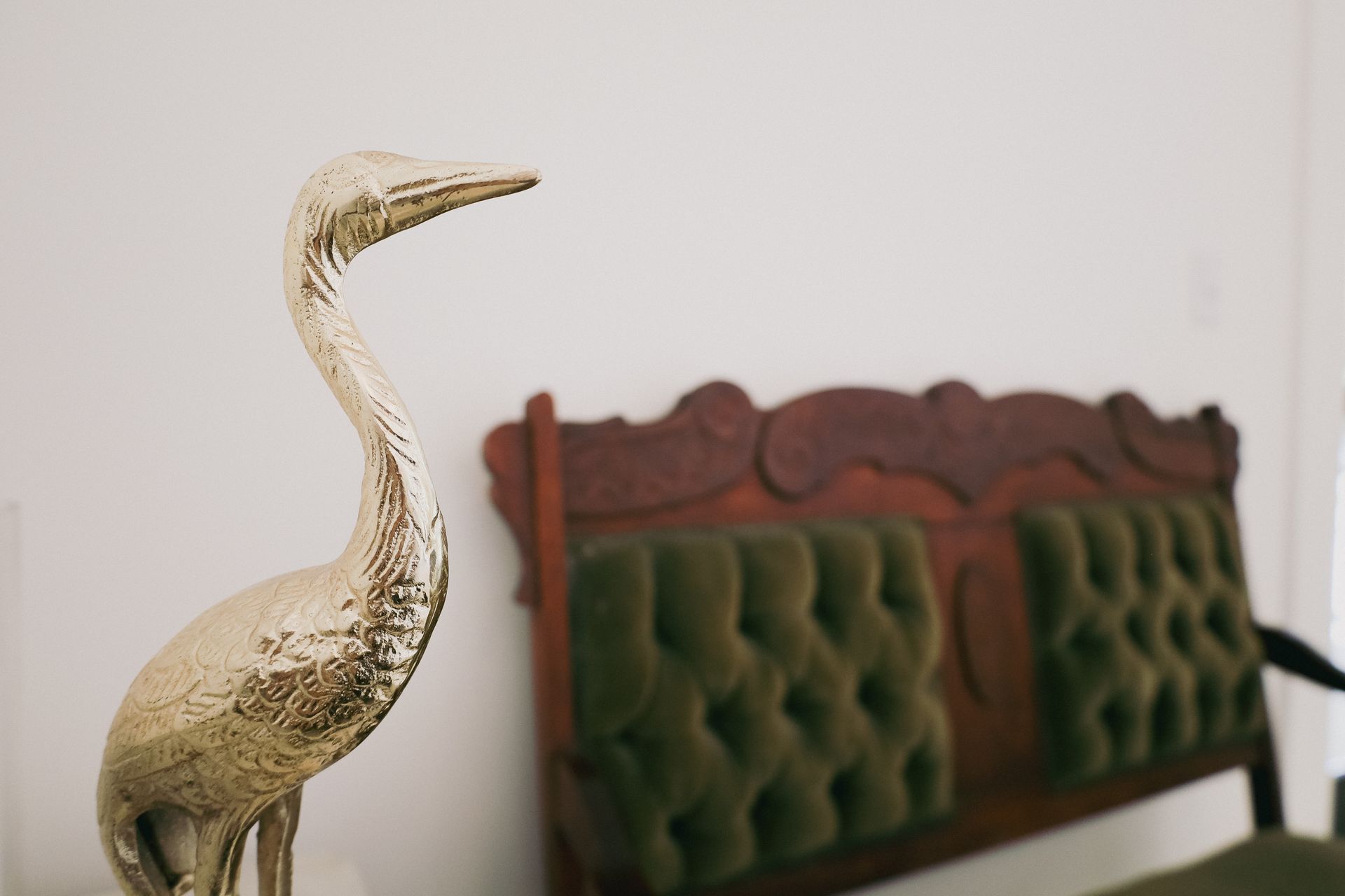 Gold heron statue in front of a tufted green and brown wooden headboard.