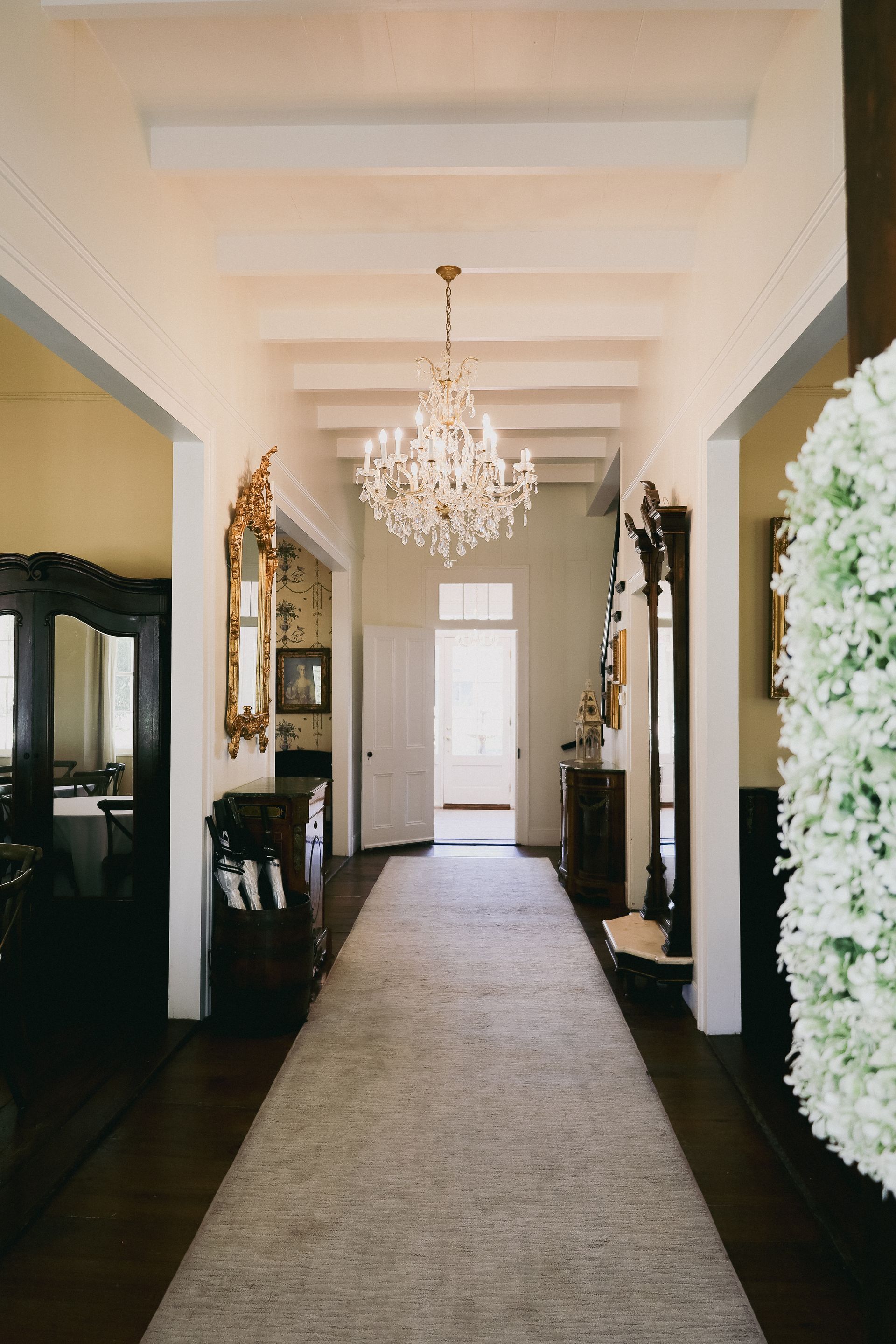 Long hallway with rug, chandelier, and various ornate decorations.