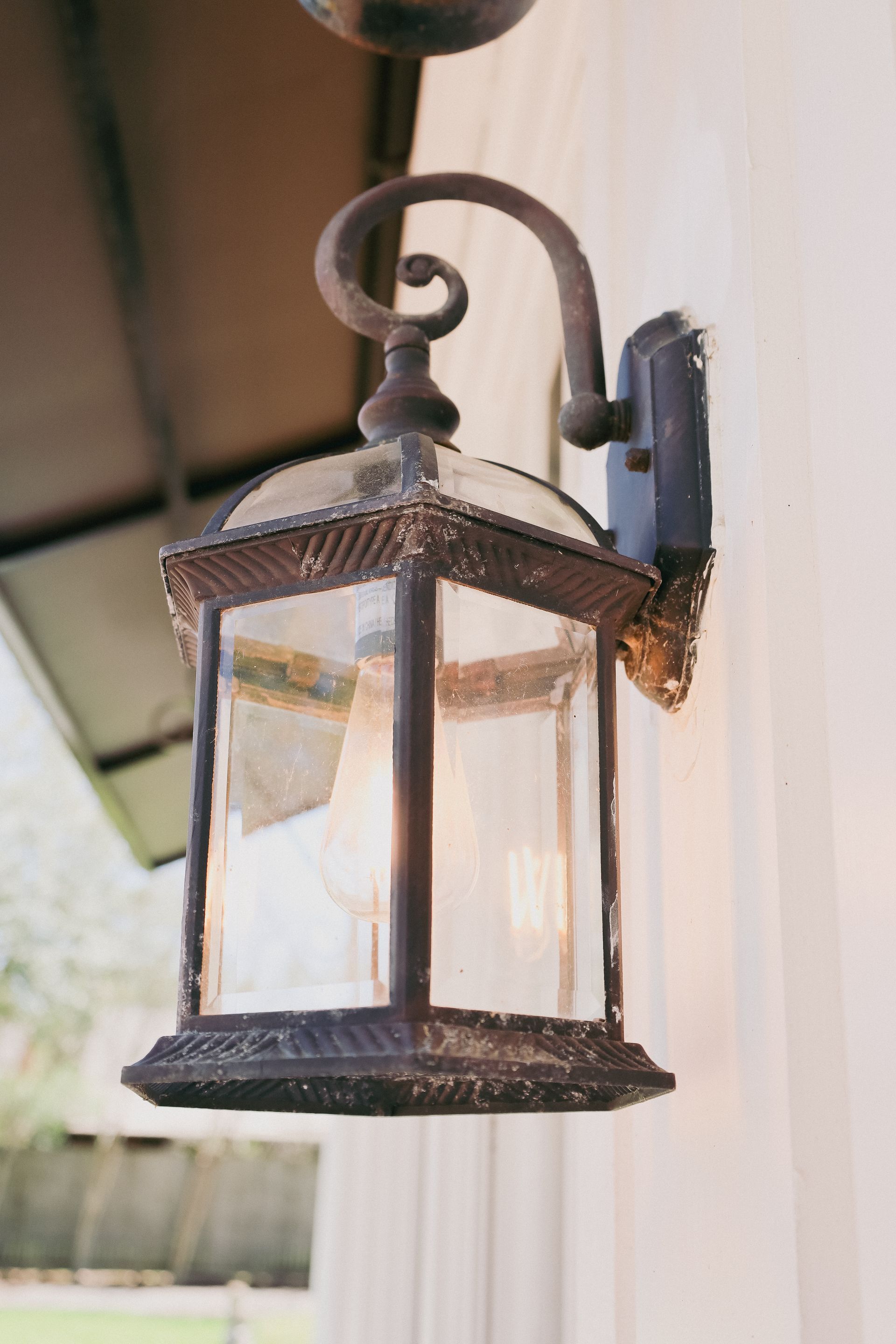 Outdoor lantern, ornate metal frame, glass panels, mounted on a white wall.