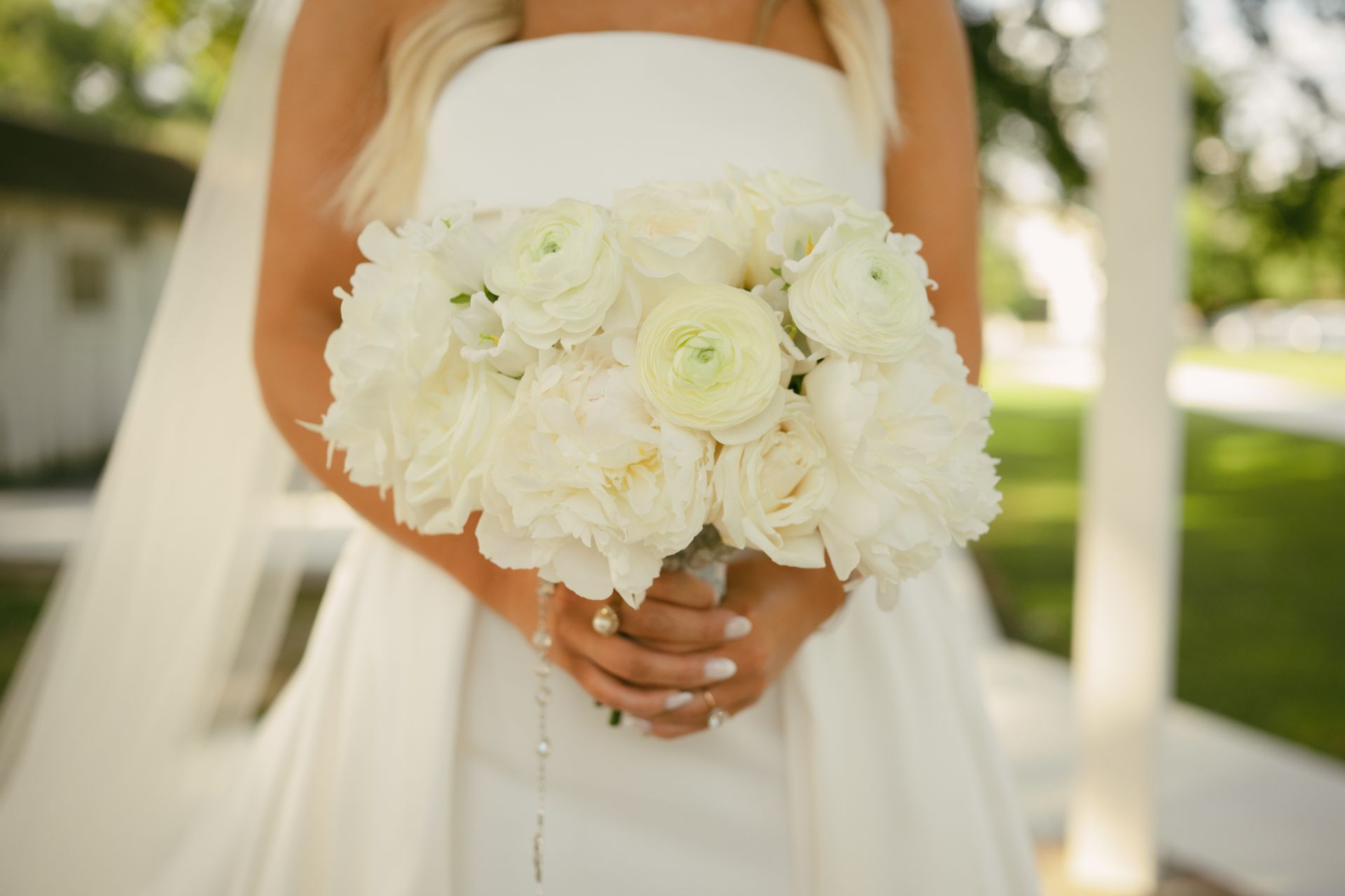 Bride holding a white flower bouquet, wearing a strapless dress and veil.