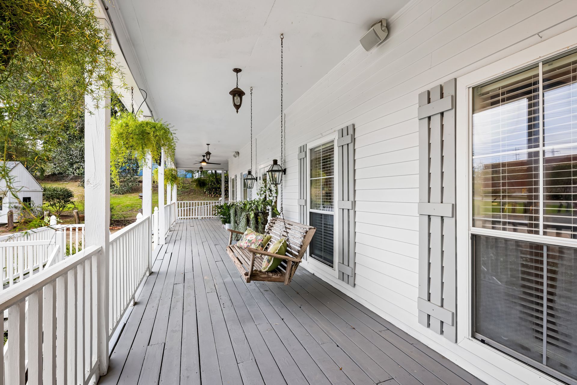 White porch with grey floor and shutters. Hanging swing and greenery.