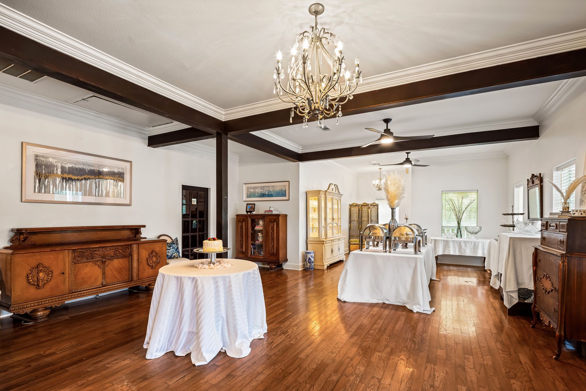 Elegant room with wood floors, tables covered in white linens, and a chandelier.