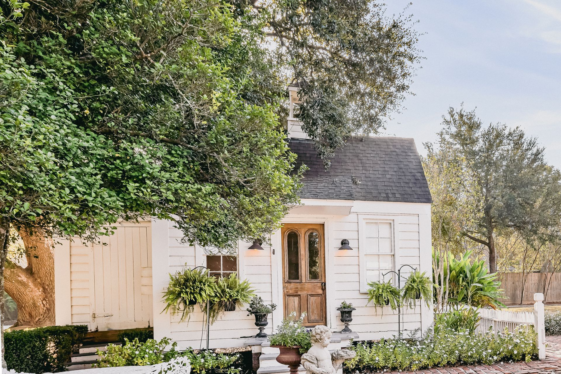 White cottage with weathered wood, brown door, and greenery.