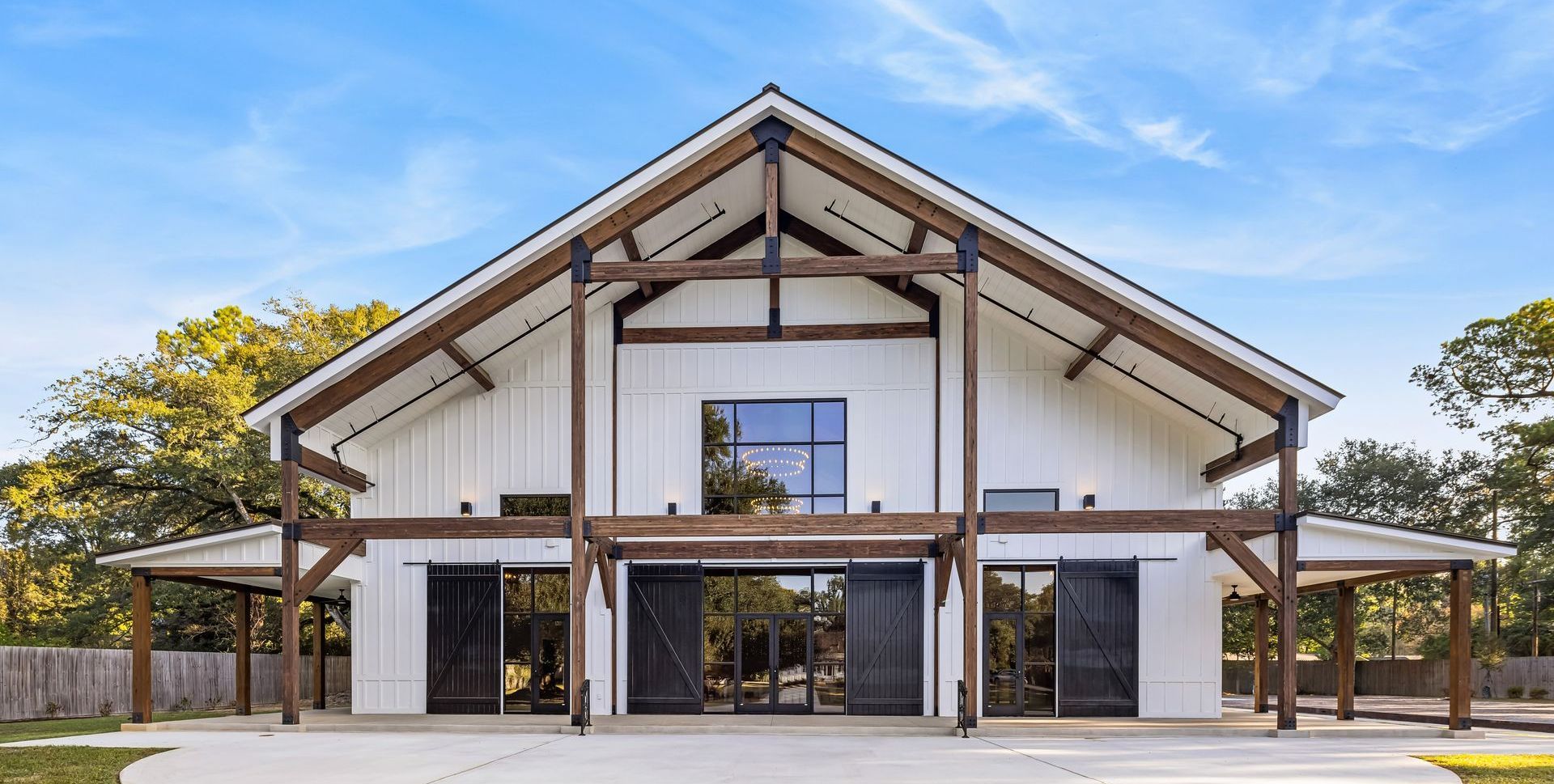 White barn-style building with exposed wooden beams, large windows, and open doors on a sunny day.