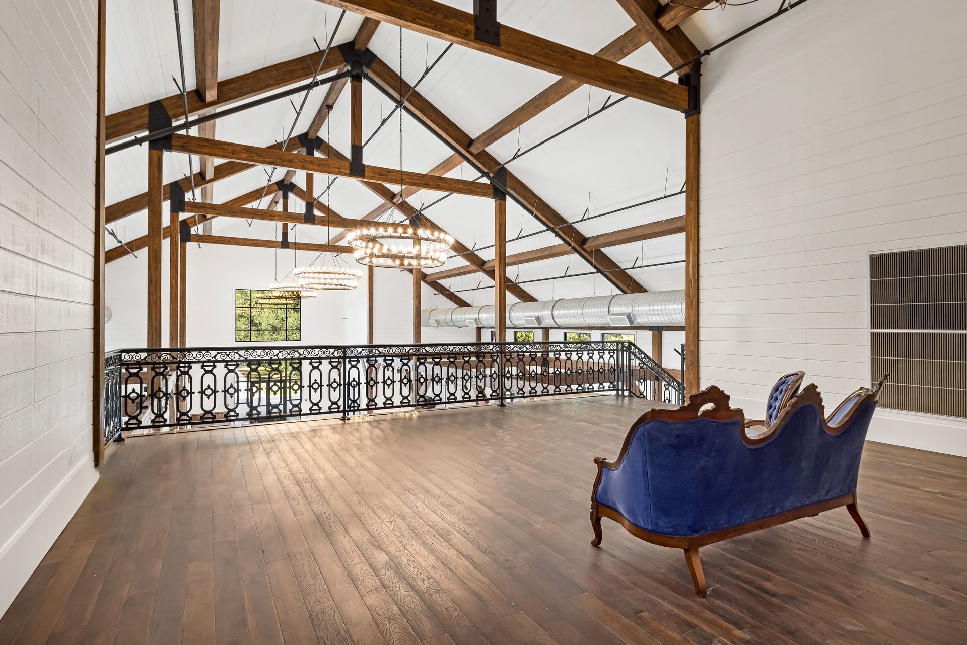 Interior of a high-ceilinged room with exposed wooden beams, a blue velvet couch, and a balcony.