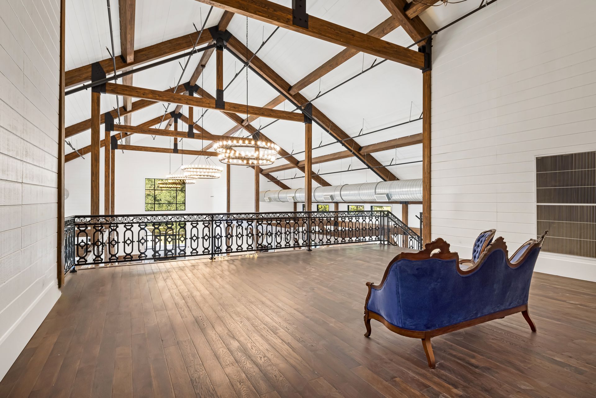 Loft with wood beams, a blue velvet couch, and a wrought-iron balcony. Bright, spacious interior.