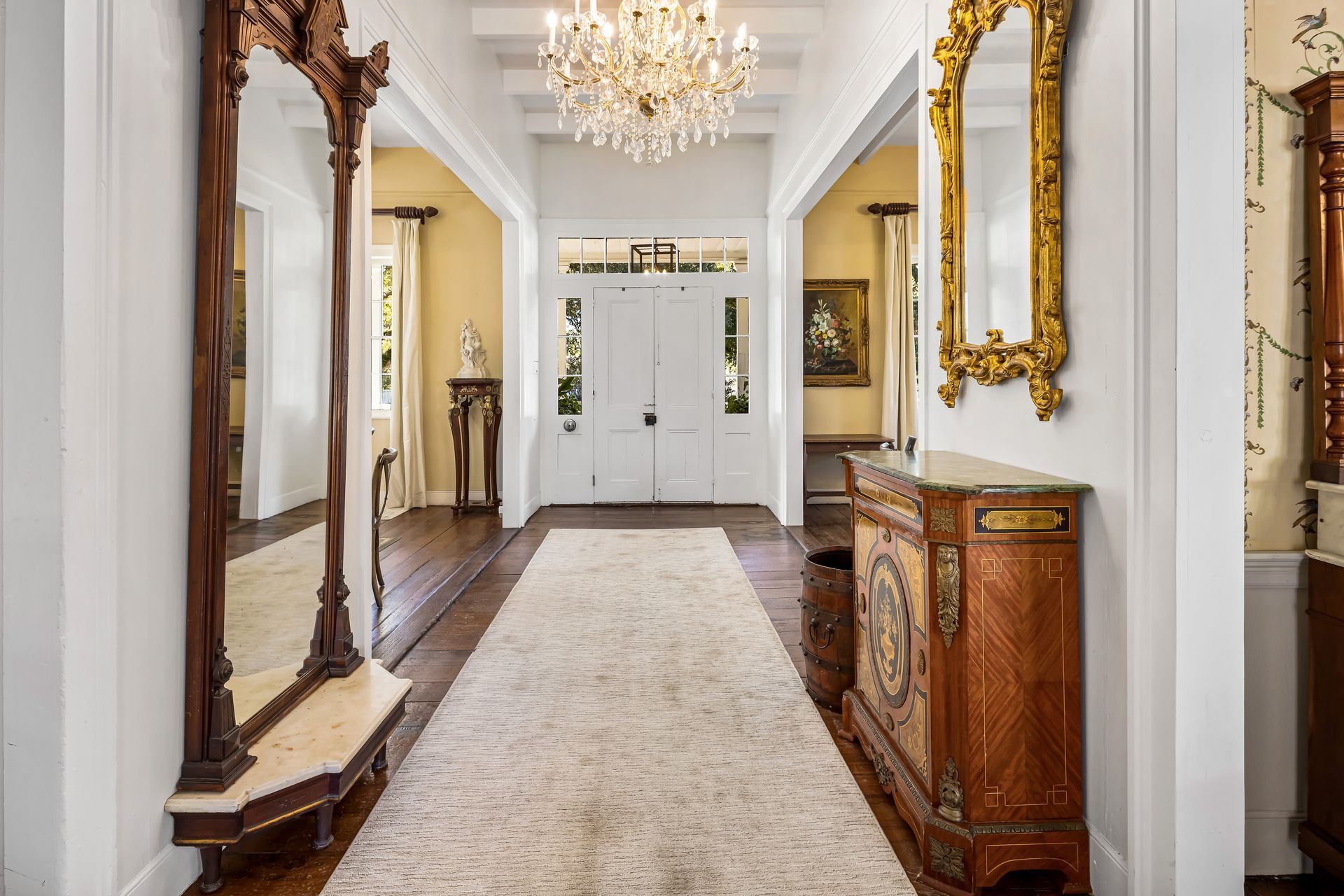 Long hallway with ornate furniture, antique mirrors, and a chandelier.