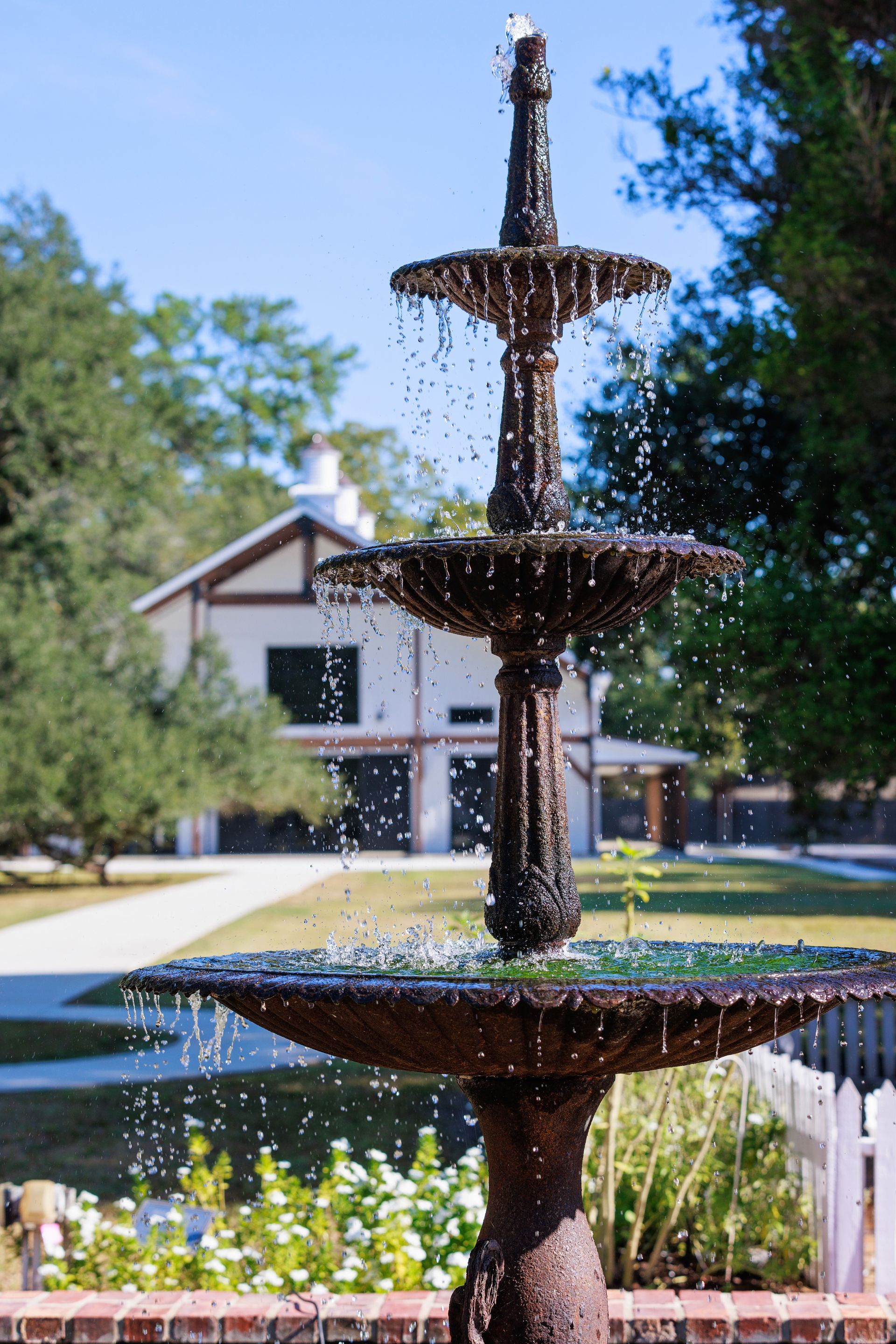 Three-tiered water fountain in front of a light-colored building under a bright blue sky.