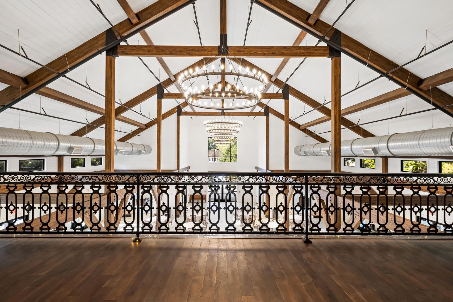 Interior view of a venue with a balcony, wooden beams, large chandeliers, and ornate railing.