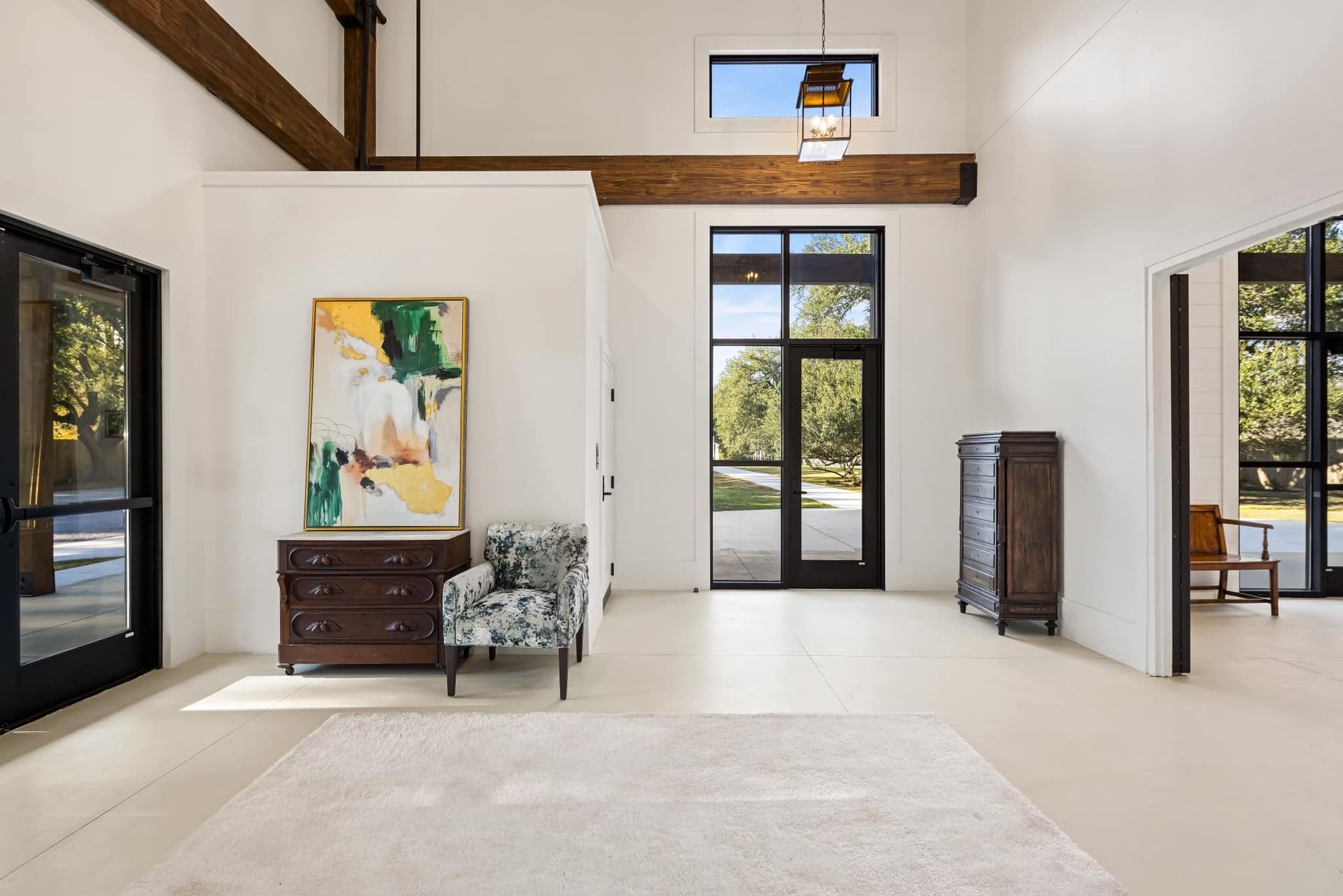 Bright white entry hall with wooden beams, dark doors and windows, rug, furniture, and abstract art.