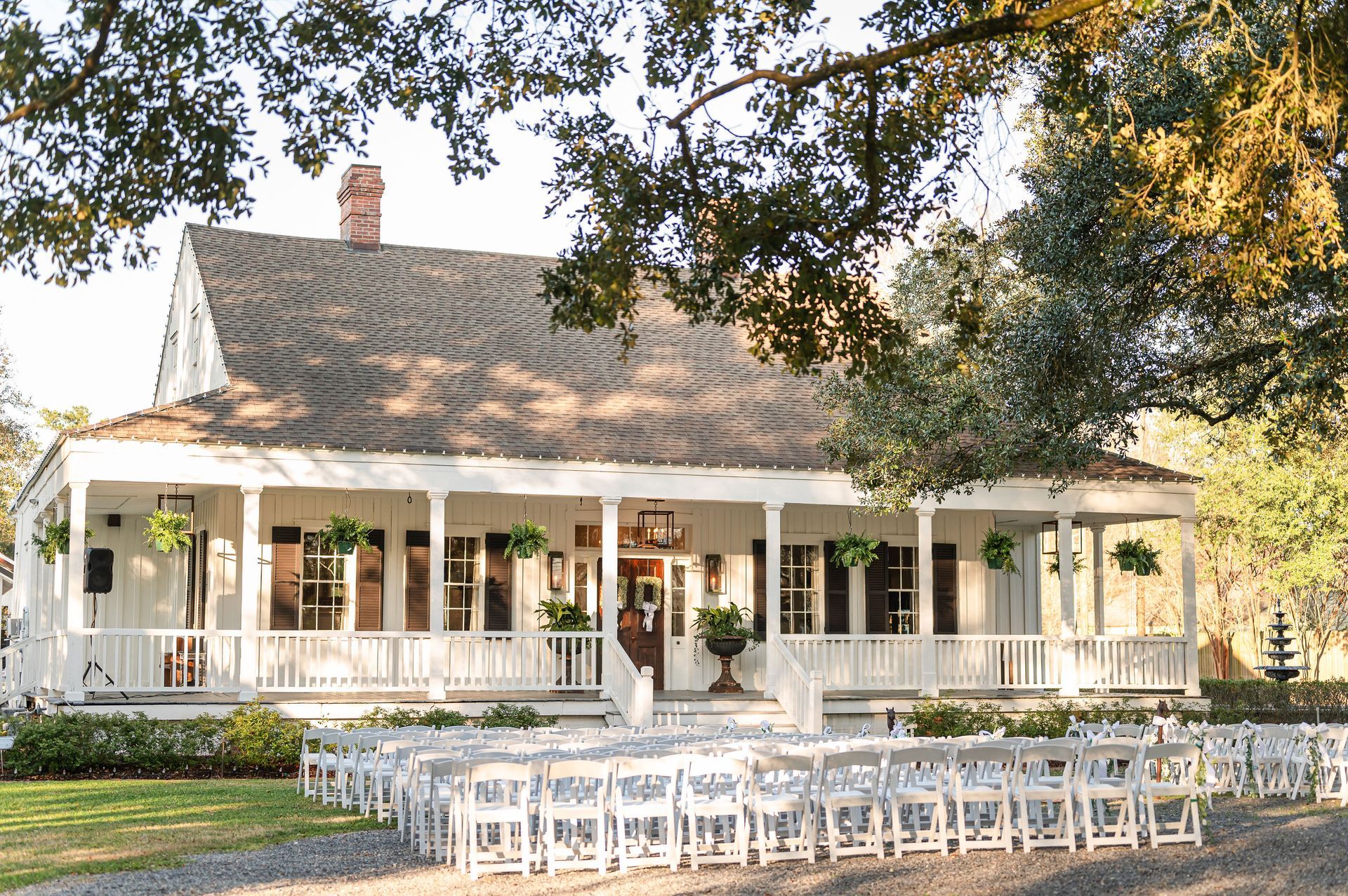White building with a long porch, set for an outdoor wedding with white chairs facing the entrance.
