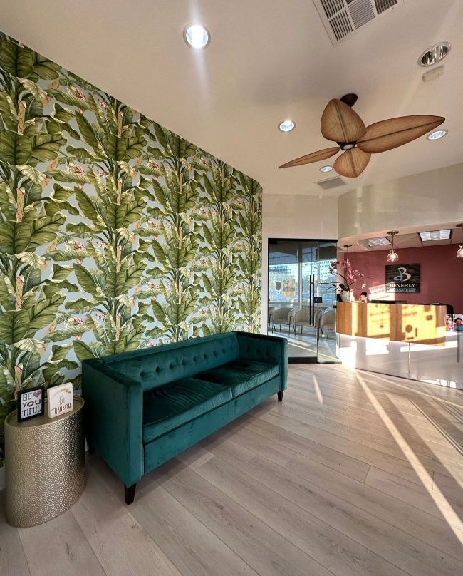 Modern lobby with teal sofa, tropical wallpaper, wood fan, and bright reception area.