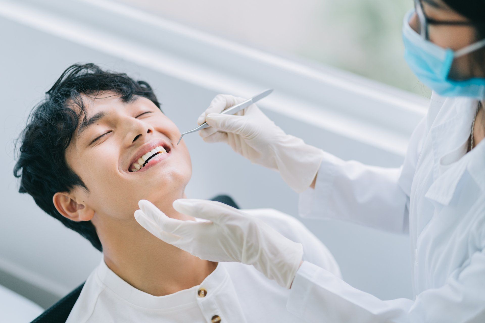 Dentist examining a smiling patient’s teeth in a bright clinic