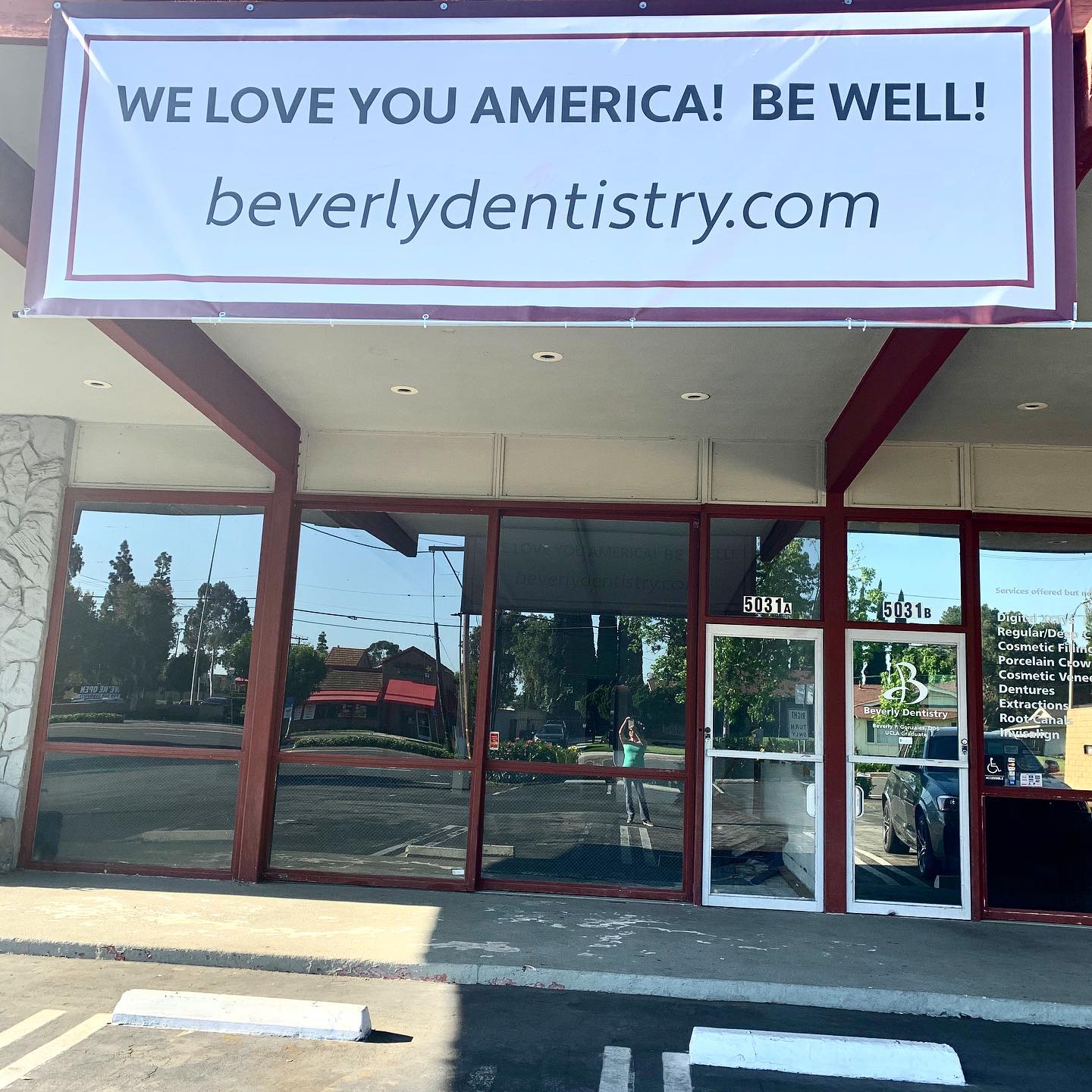 Storefront with “We love you America! Be well!” banner and beverlydentistry.com sign above the entrance