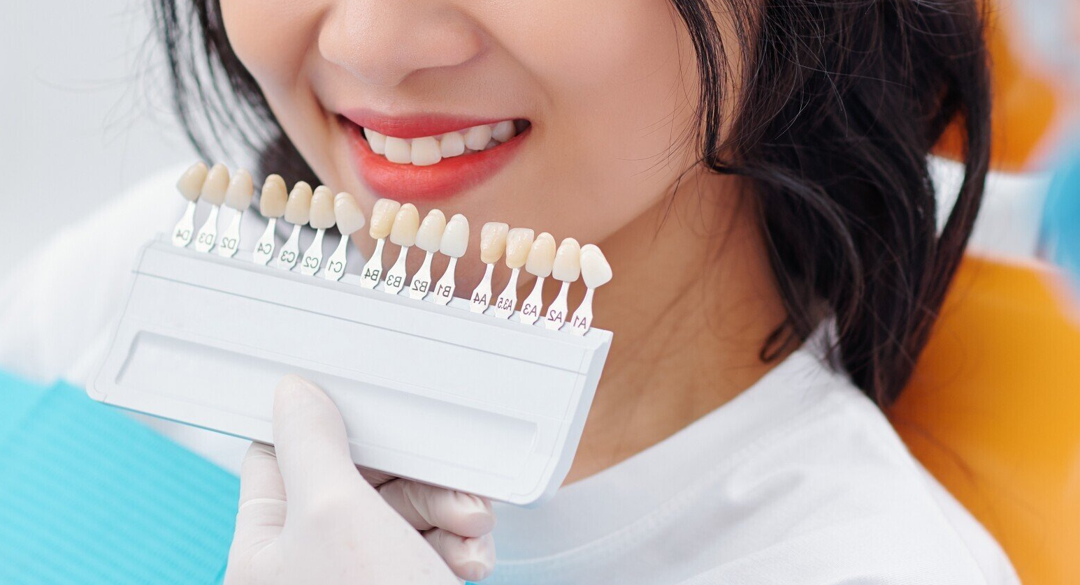 Close-up of a person smiling while choosing a white tooth shade guide with gloved hands