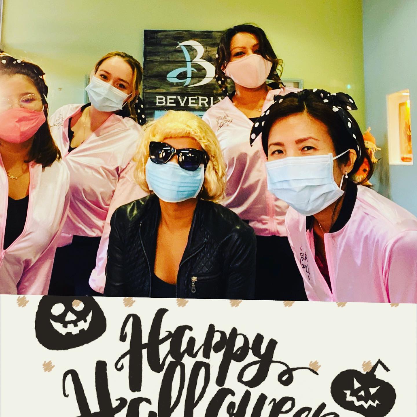 Five people in masks pose for a photo in front of a “Happy Halloween” sign.