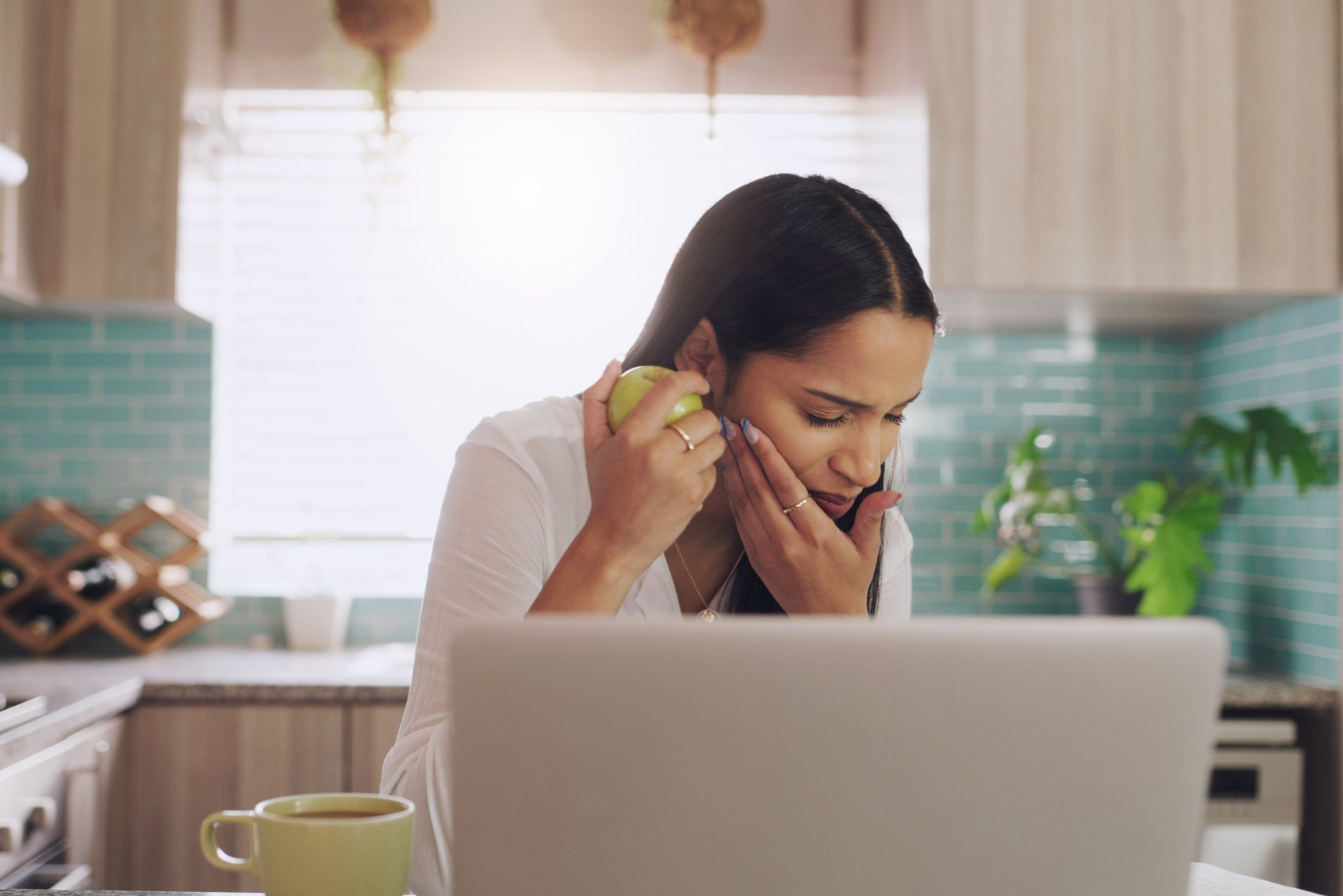 Woman at a kitchen table talking on the phone beside a laptop and mug