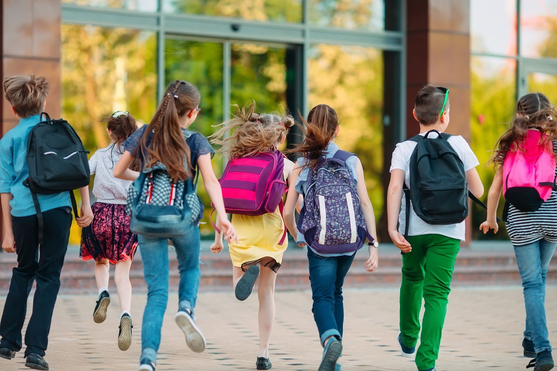 Children with backpacks walking toward a school building