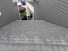 View from a roof of grey shingles looking between two green-sided walls toward a porch and plants.