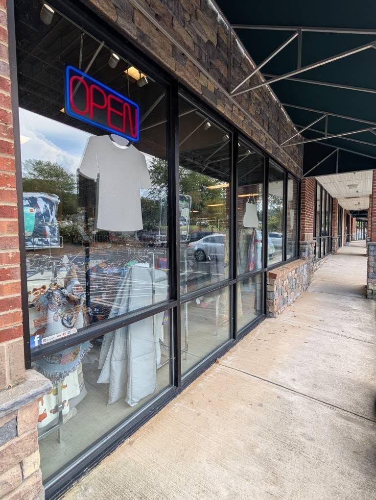 A storefront with an open sign. A white t-shirt hangs in the window.