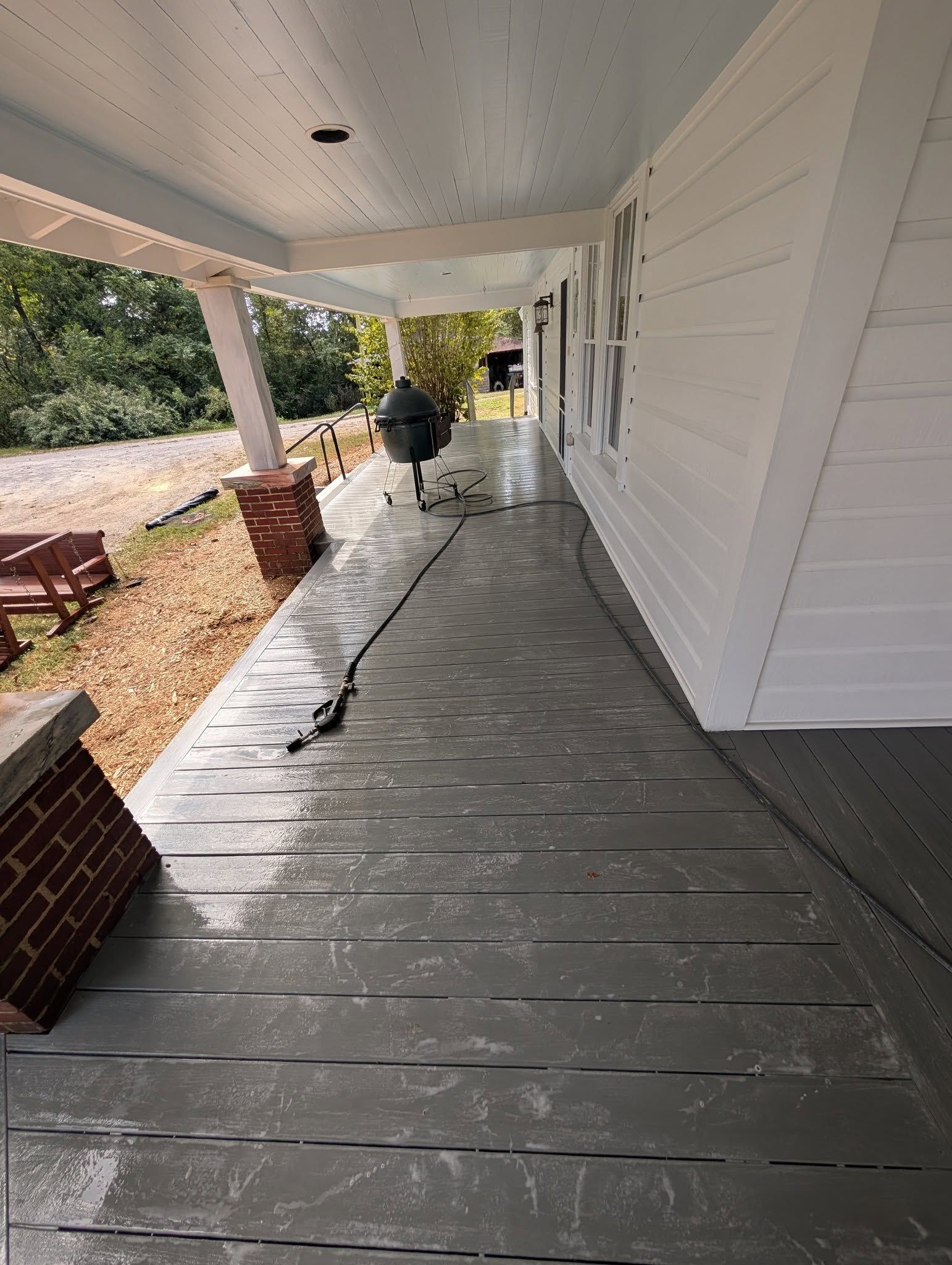 Covered porch with gray plank flooring. White siding and ceiling. Brick columns.