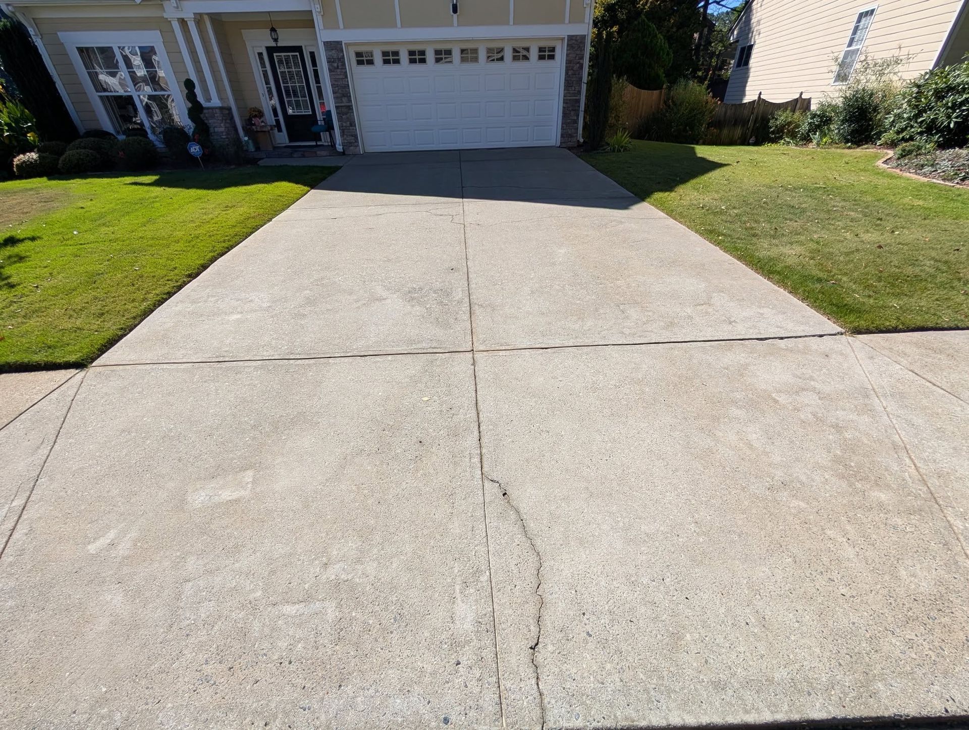Concrete driveway leading to a white garage, flanked by green grass. House in the background.