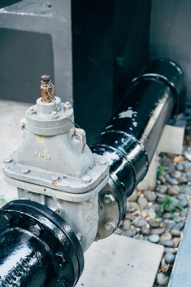 Black and gray water valve attached to a large black pipe, outdoors.