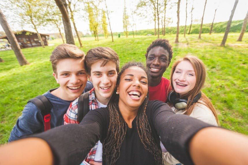 Group of diverse teens smiling for a selfie in a park.