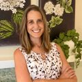 Smiling woman in a floral sleeveless top standing before floral wall art and greenery