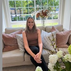 Woman sitting on a beige couch in a bright living room with pink and white pillows and flowers nearby