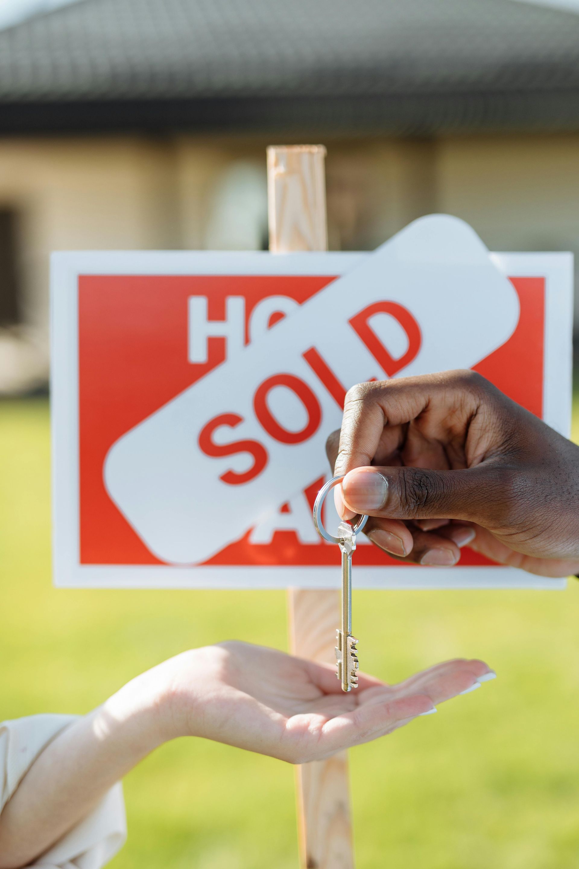 Hand placing house key into another hand, with a red 