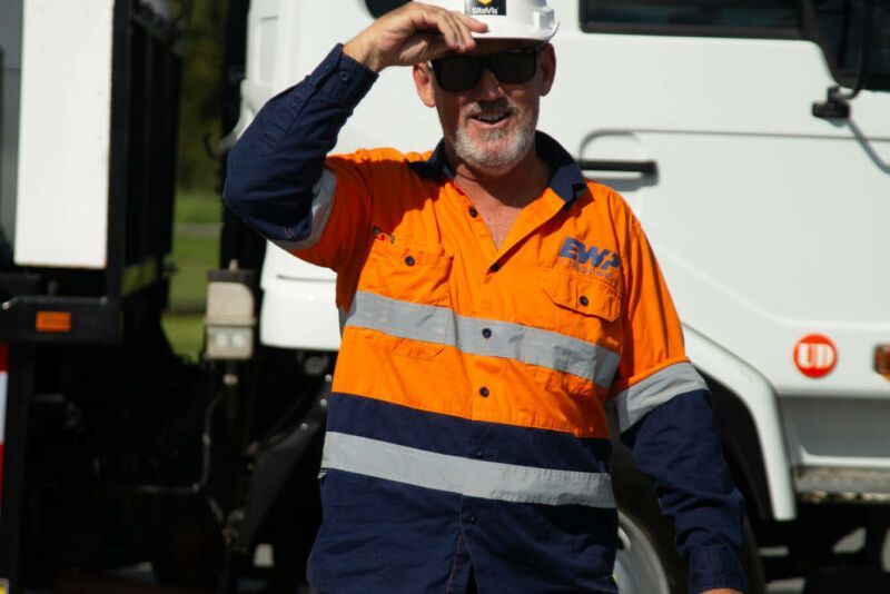 A man wearing a hard hat and sunglasses is standing in front of a truck