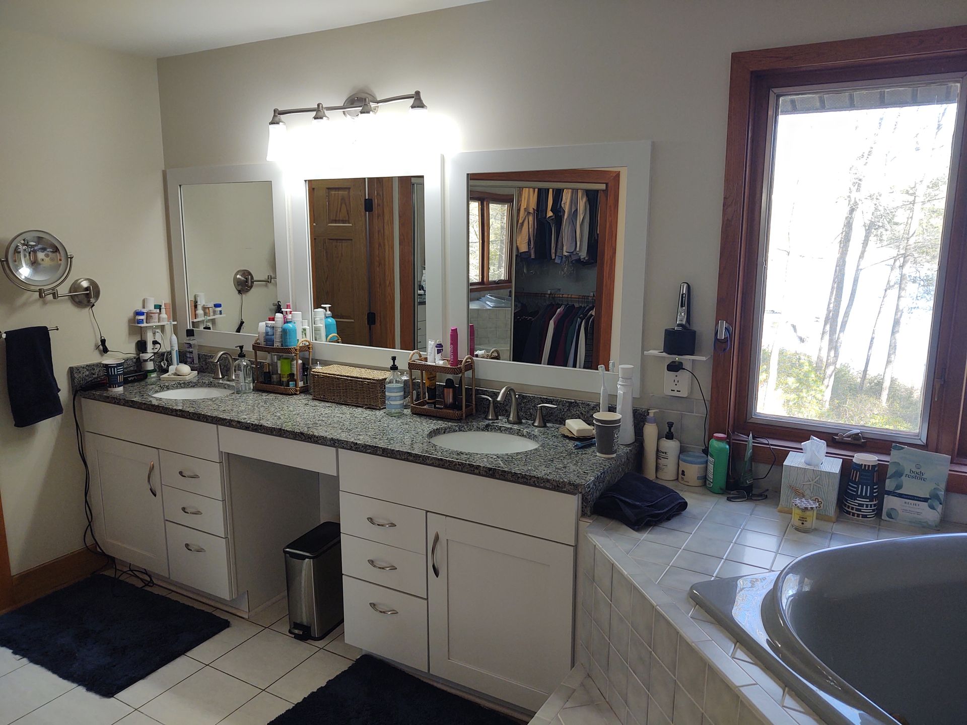 Bathroom with double vanity, two mirrors, and window overlooking trees and a body of water.
