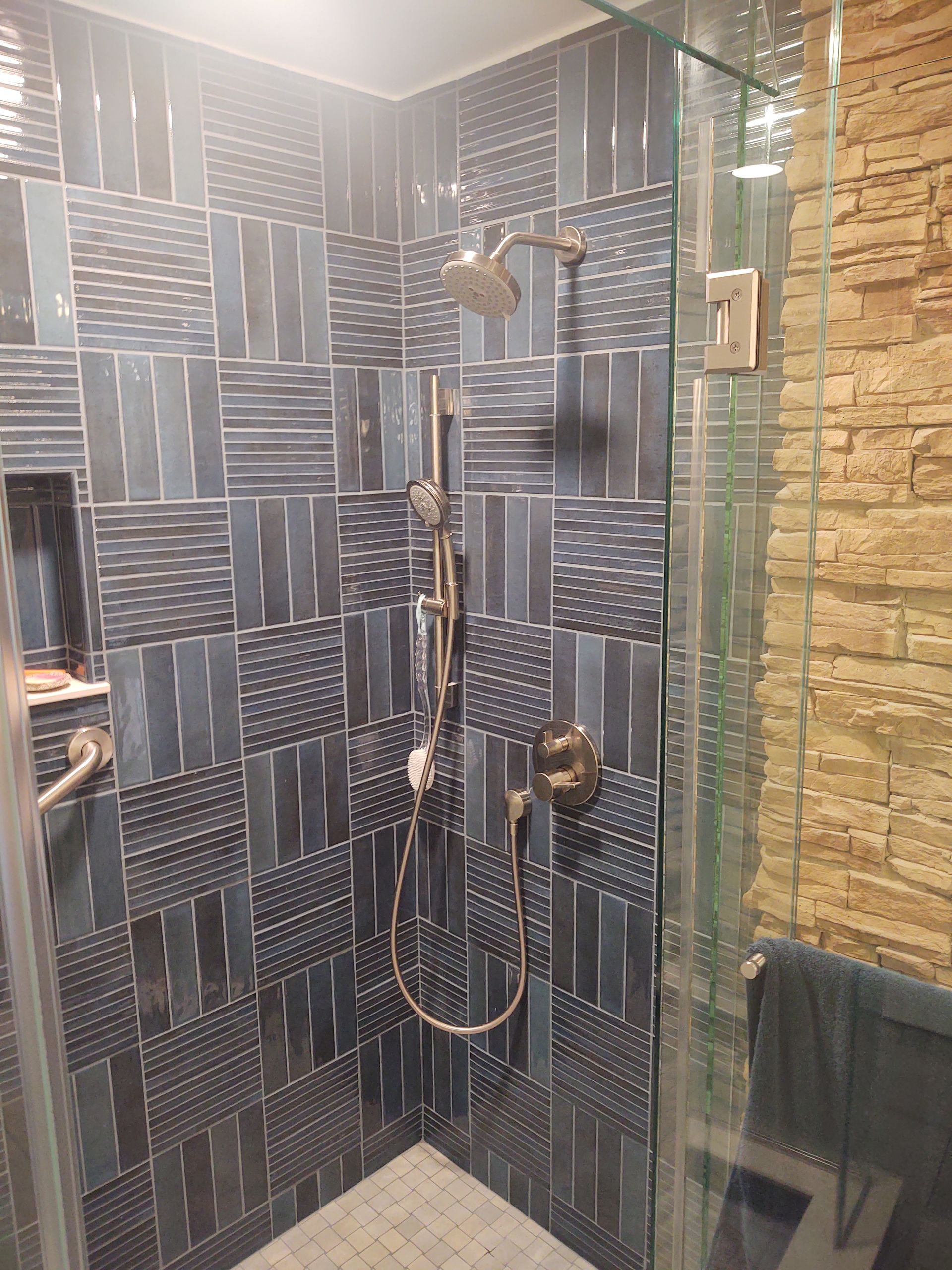 Shower with blue patterned tile, glass enclosure, and stone accent wall.