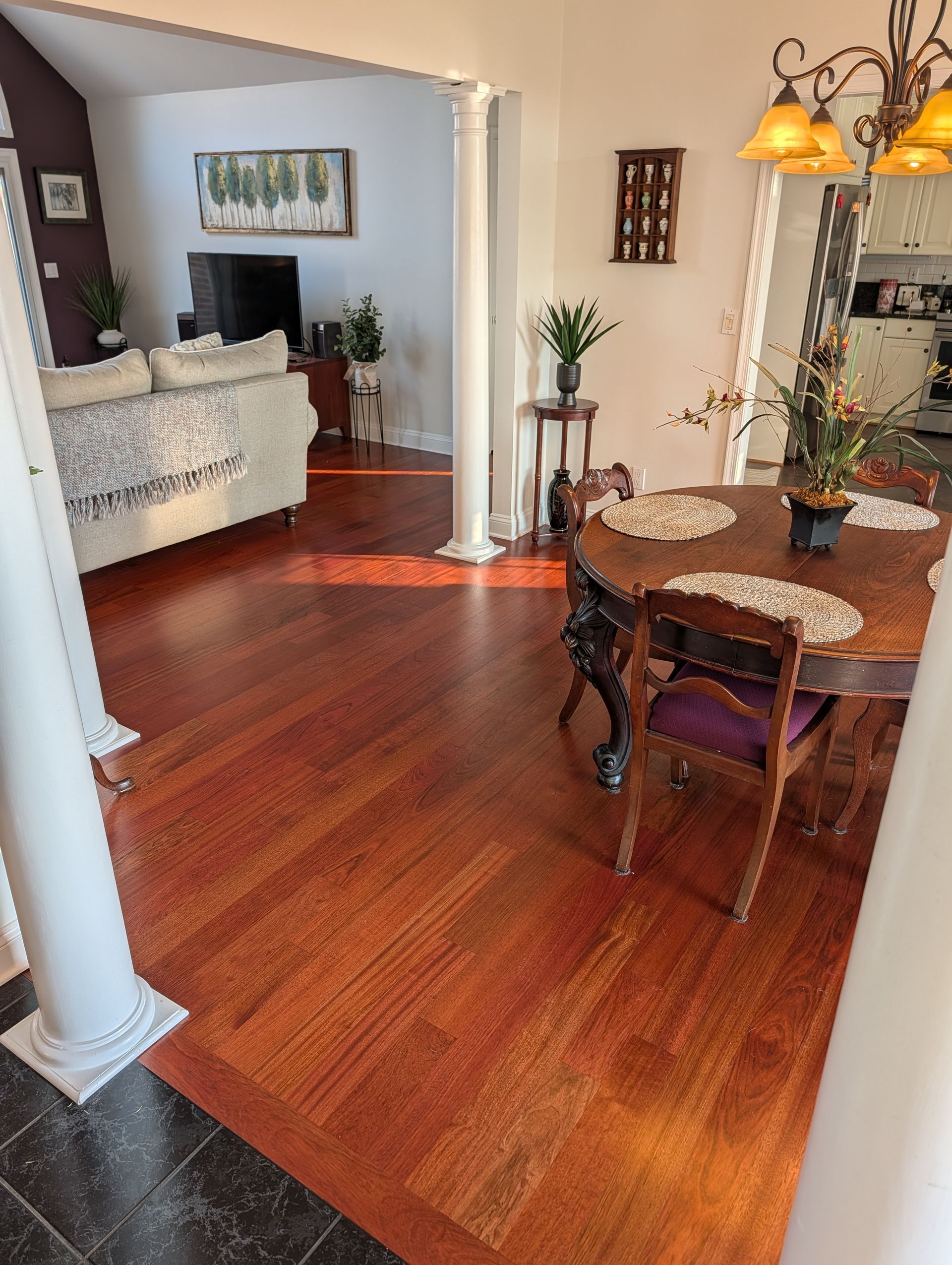 Dining area with red wood floors, round table, chairs, pendant lights, and a view into a living room