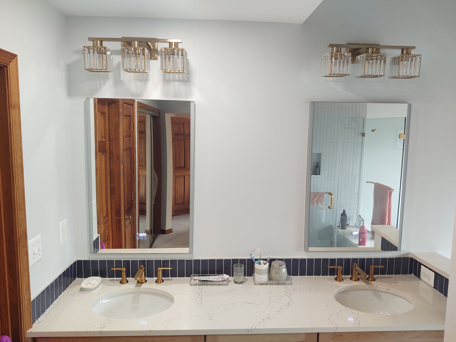 Bathroom with two mirrors, light fixtures, two sinks, and a light blue wall.