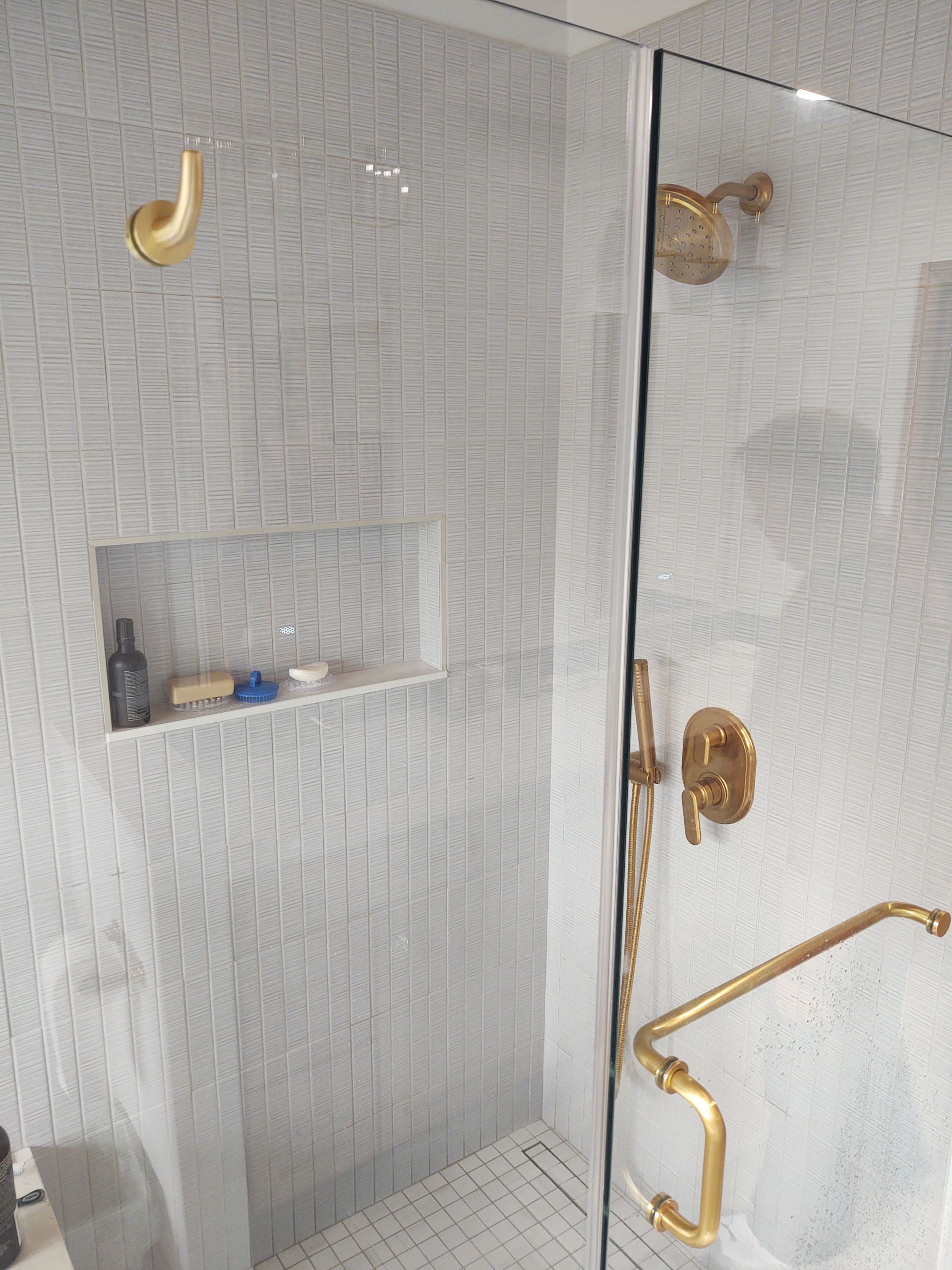 Shower with gold fixtures and white tile.