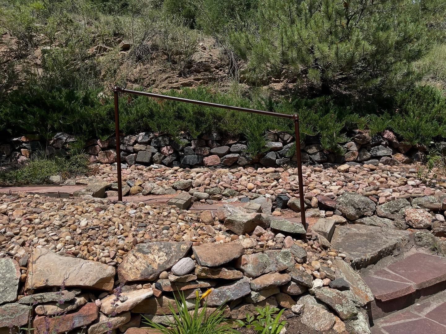 Metal frame on a rocky landscape, with stone walls and green foliage in the background.