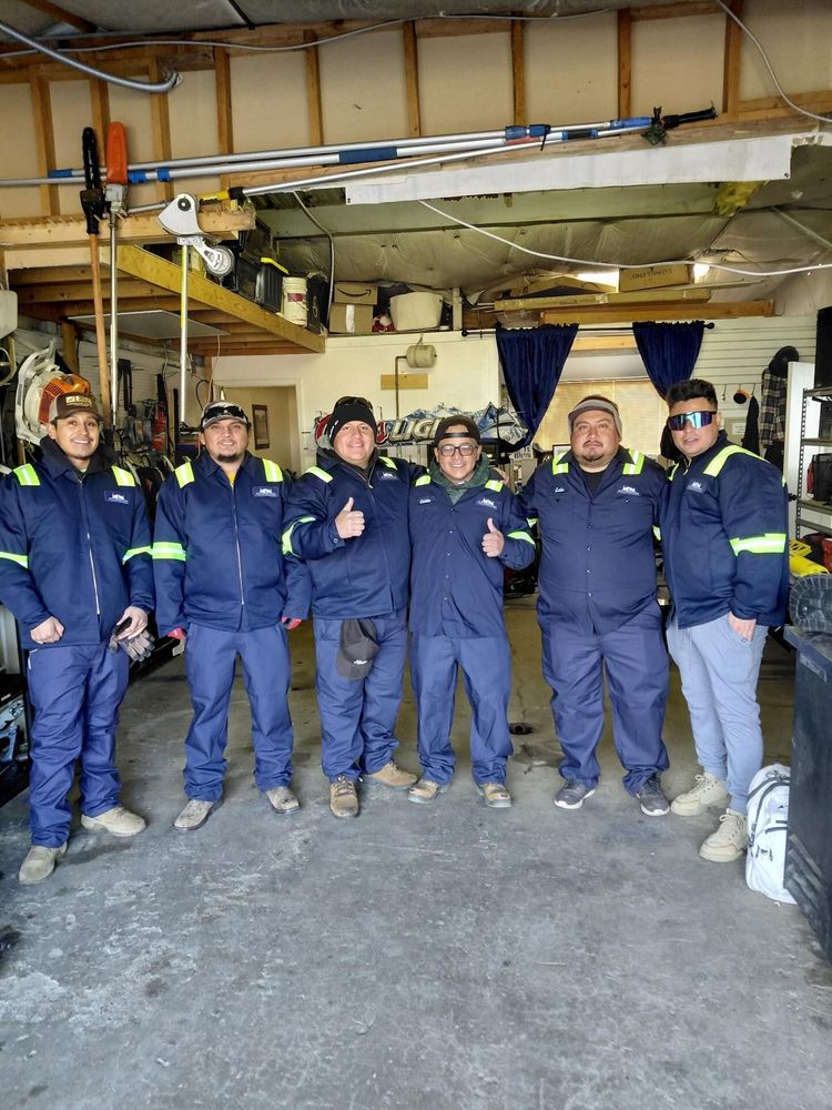 Six people in blue work uniforms pose in a garage, several give a thumbs up.