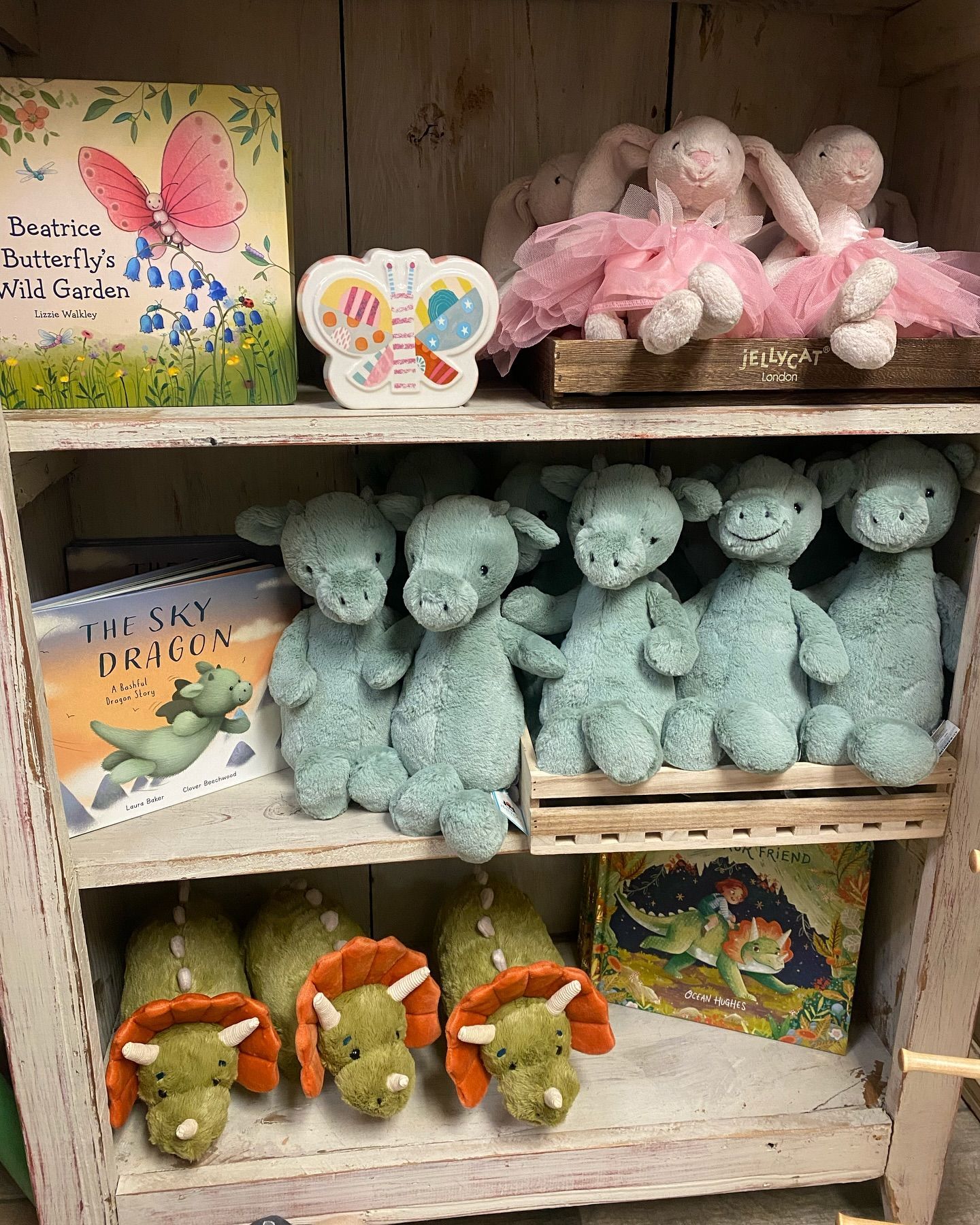 White shelf display filled with plush toys and books, including bunnies, dragons, and triceratops.