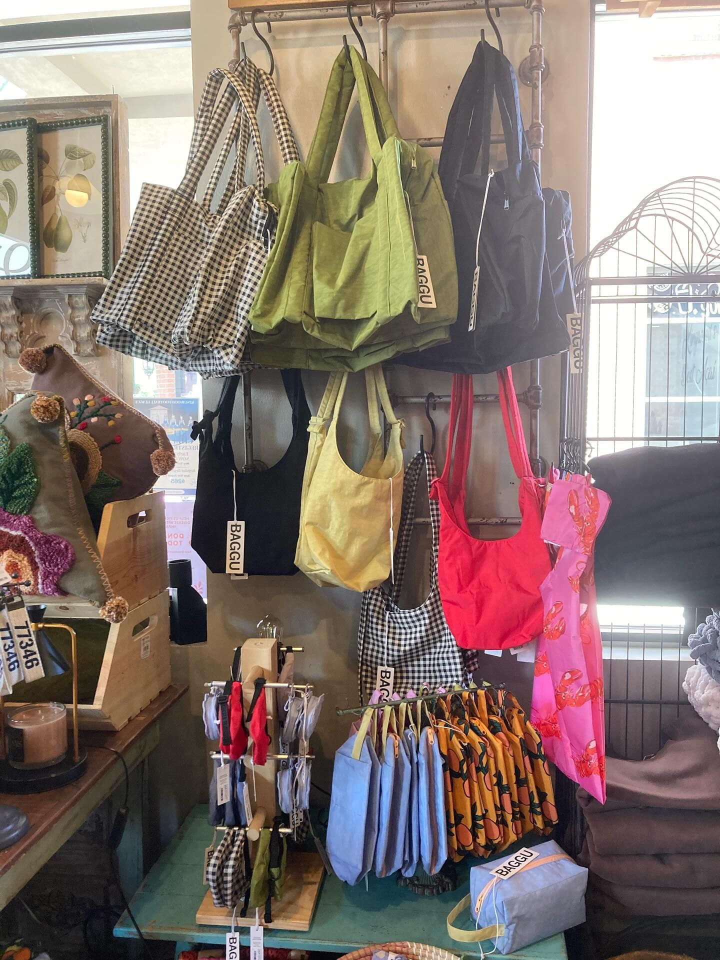 Display of colorful tote bags hanging in a shop. Includes black, green, yellow, and patterned bags.