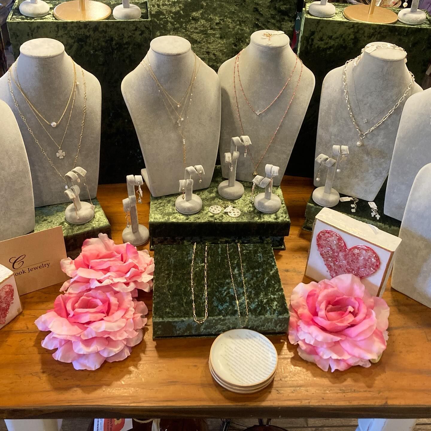 Jewelry display with necklaces and earrings on mannequins, pink roses, and marble platforms.