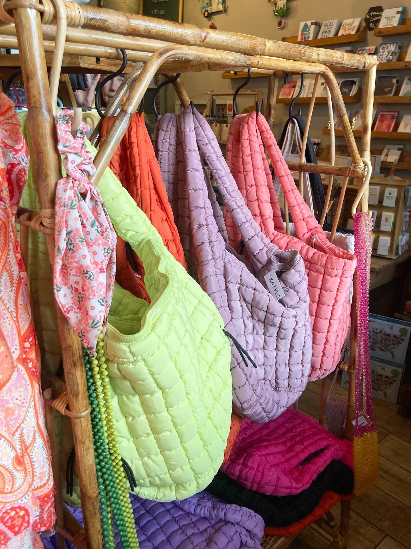 Bags in various colors, including lime green, orange, purple, and pink, hang on a bamboo rack in a shop.